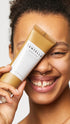 Person holding a skincare product with a visible brand name against a neutral background